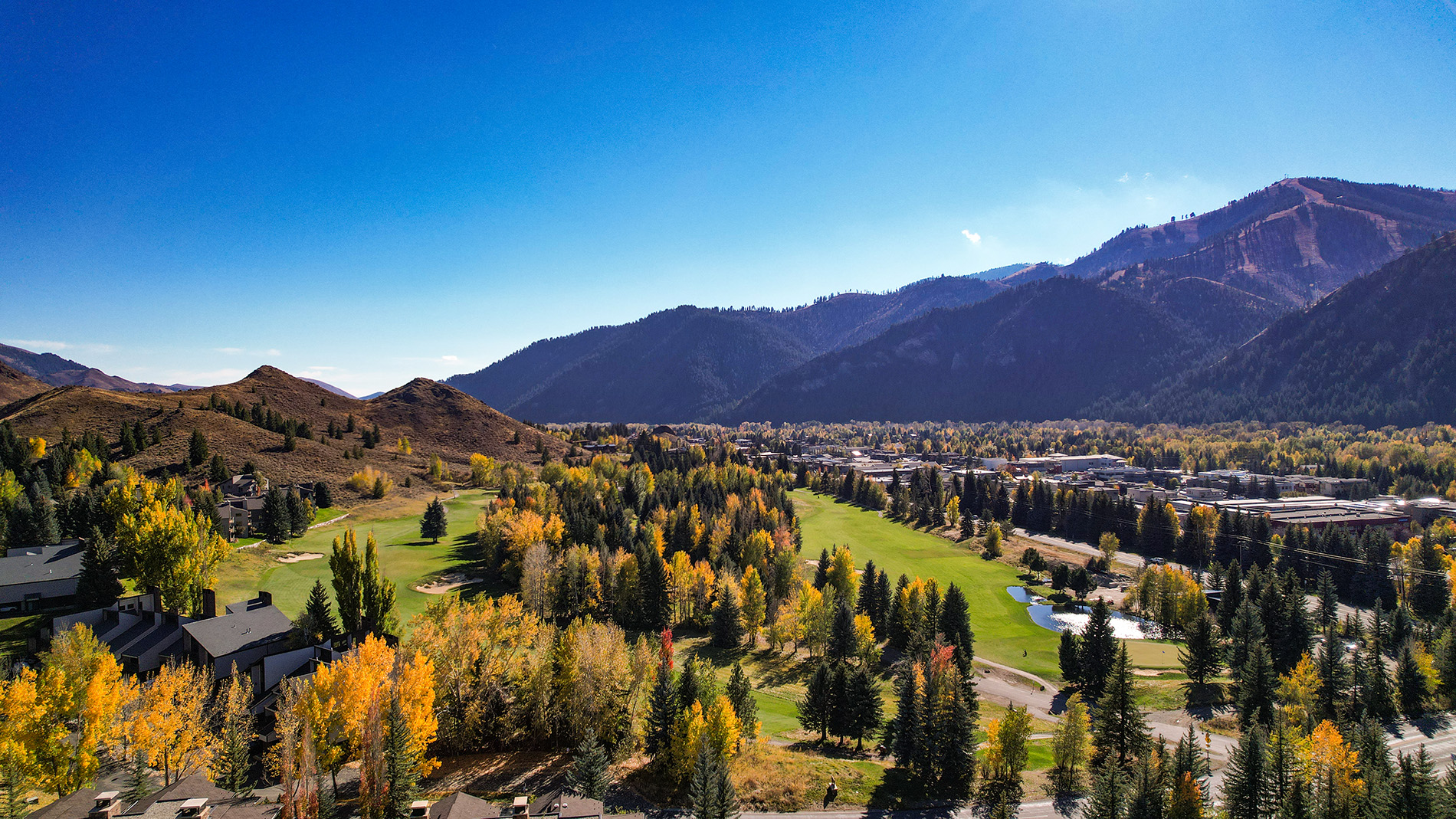 Aerial view of Bigwood Golf Course in fall, with mountains behind it