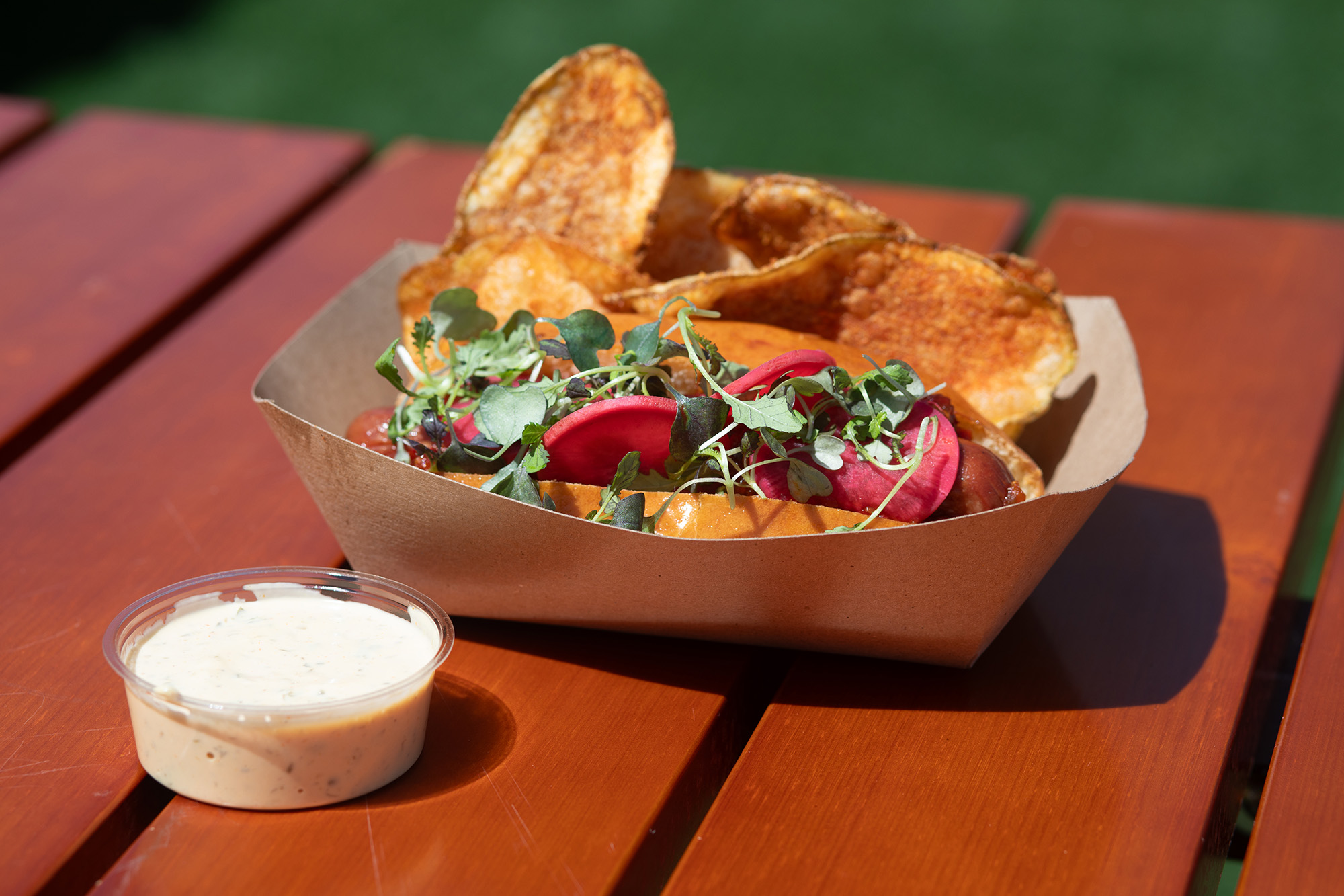 Hot dog in a paper boat with chips and dipping sauce